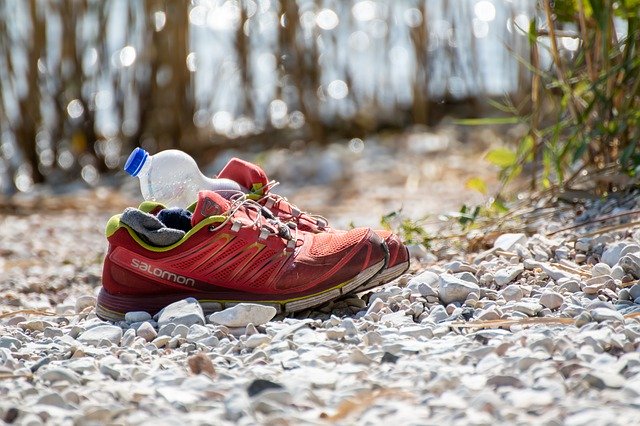 Et par røde Salomon løbesko med en tom vandflaske i den ene sko, der står på en grussti